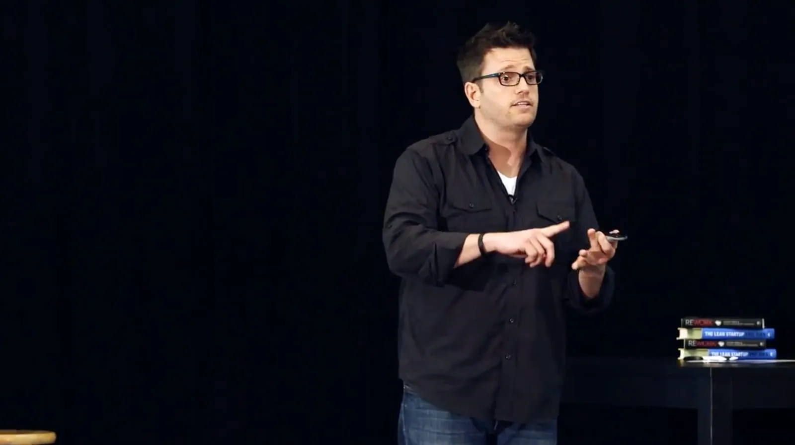 Rob Scott speaking on stage, at ease, with his books beside him